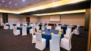 Un salón de conferencias con mesas redondas, sillas blancas y manteles azules.