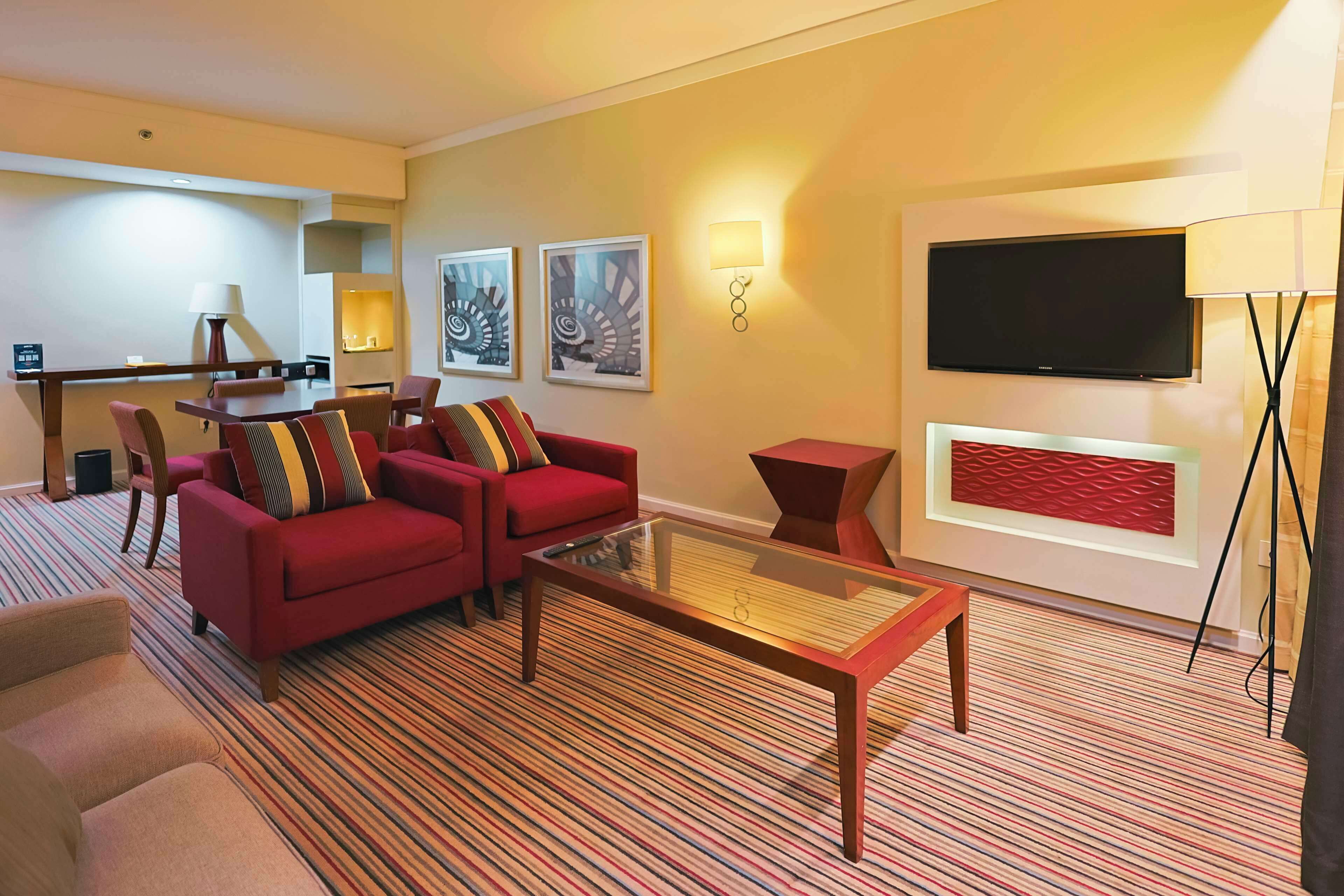 A hotel room with a red sofa, a glass coffee table, a TV, and a small side table.
