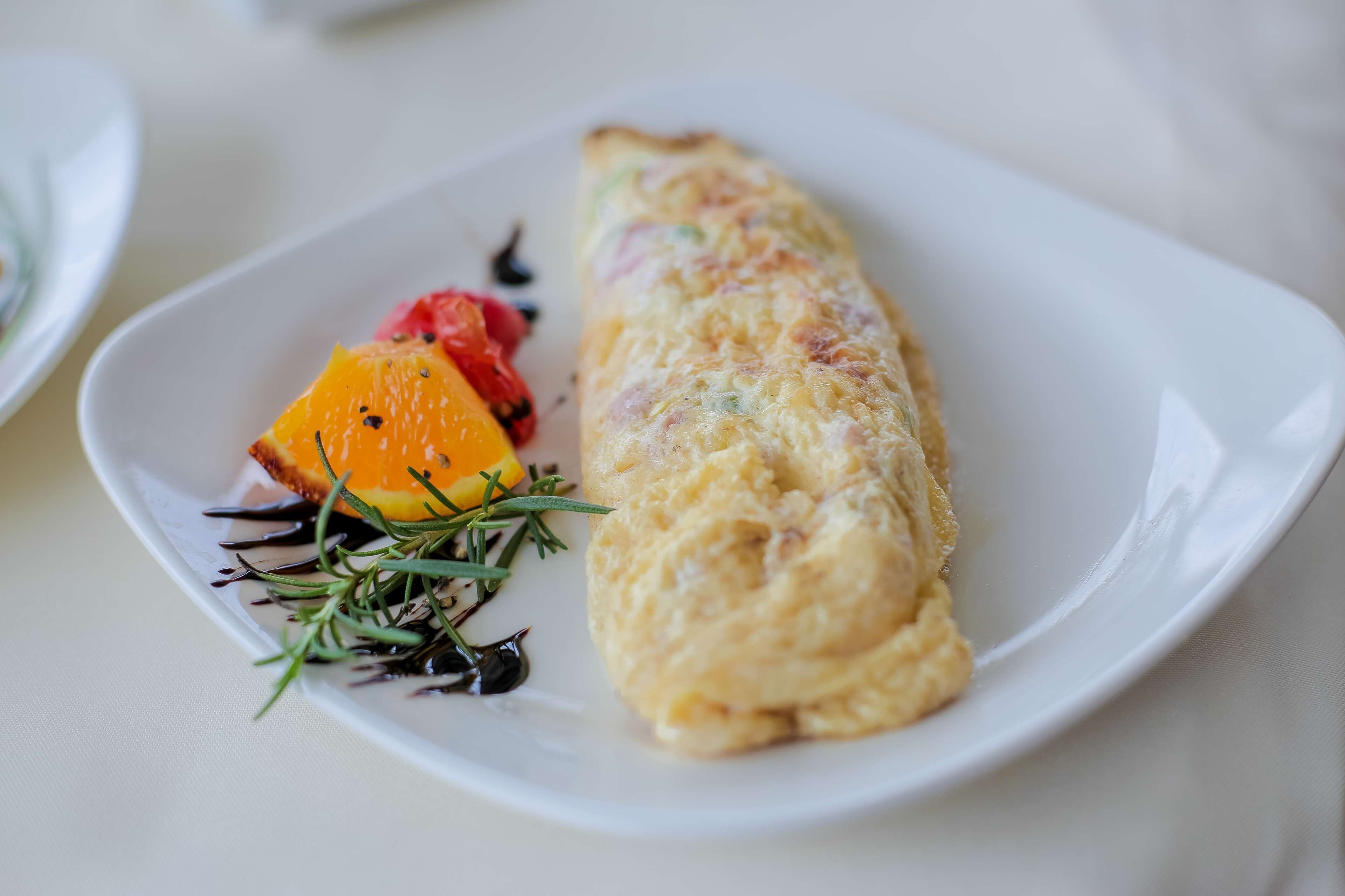 A plate with an omelette, orange slice, and some greens.