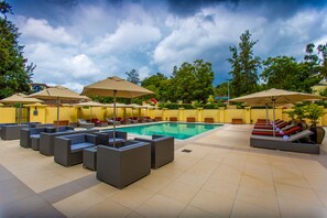 A poolside area with lounge chairs and umbrellas, a swimming pool, and a yellow building in the background. - Park Inn by Radisson Kigali (Kigali)