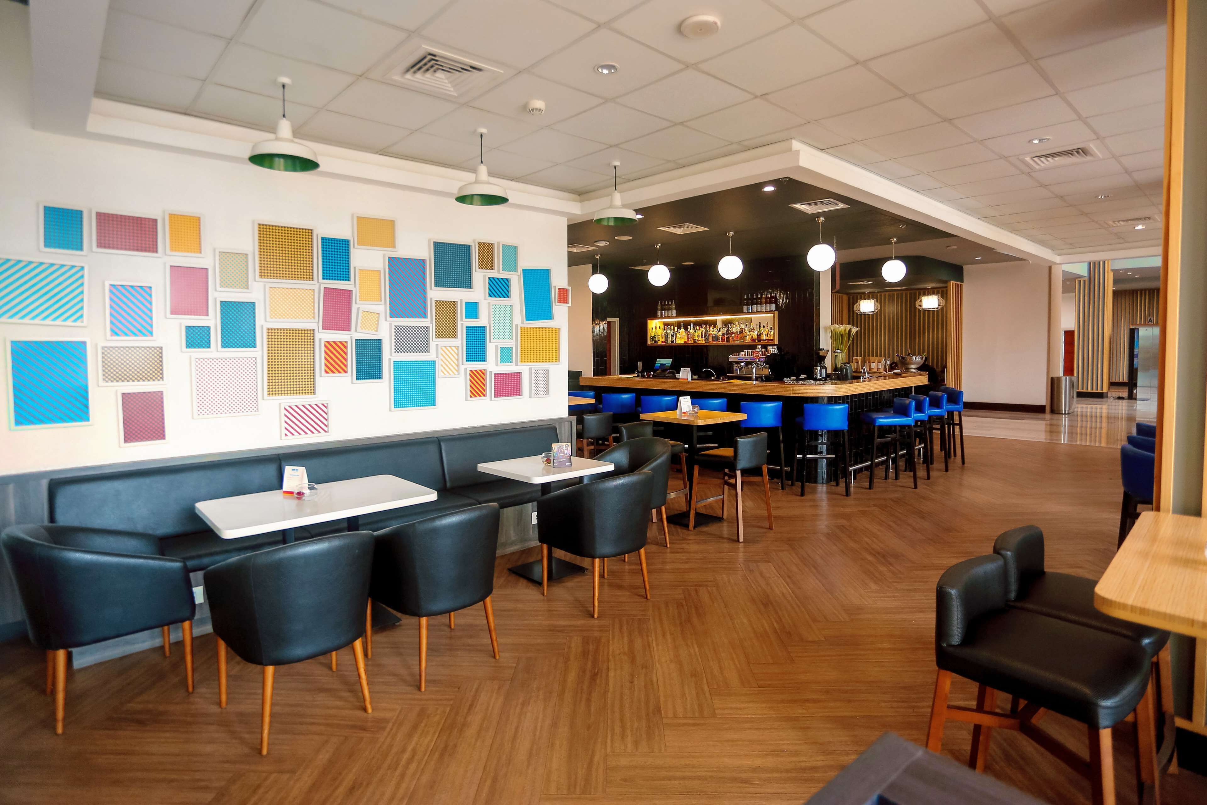 A modern restaurant with a bar area, wooden flooring, and black upholstered chairs.