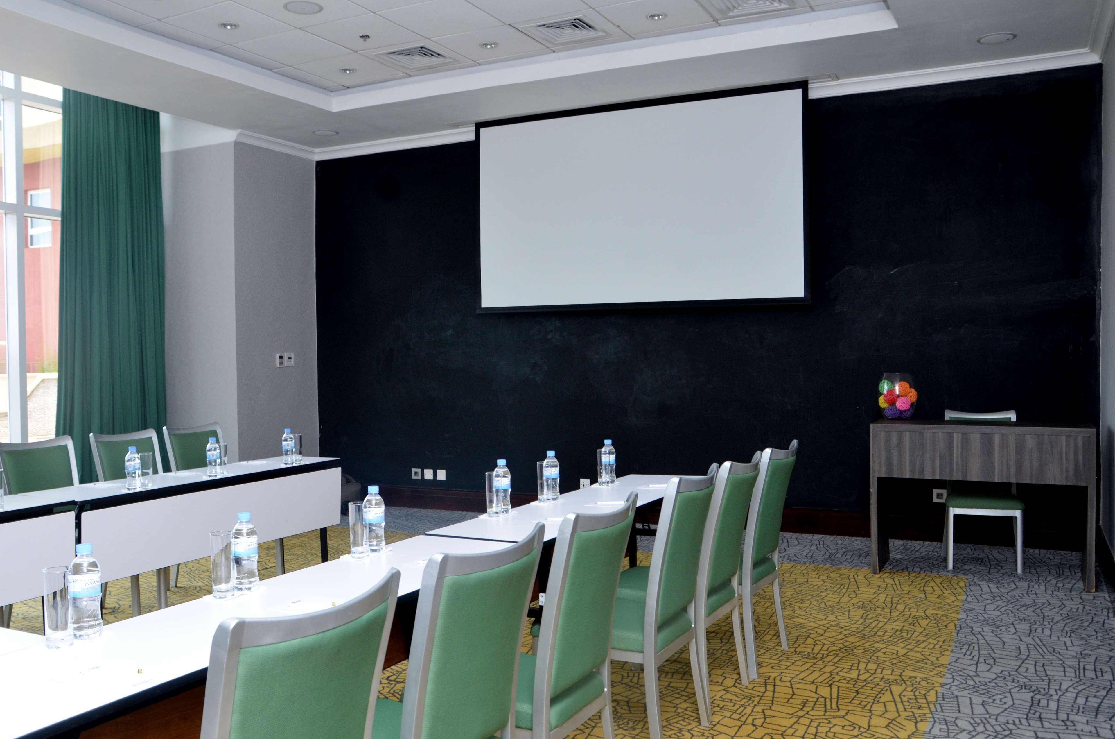 A conference room with a long table, chairs, a projector screen, and a small table with a vase of flowers.