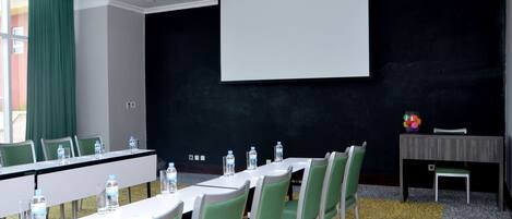 A conference room with a long table, chairs, a projector screen, and a small table with a vase of flowers.
