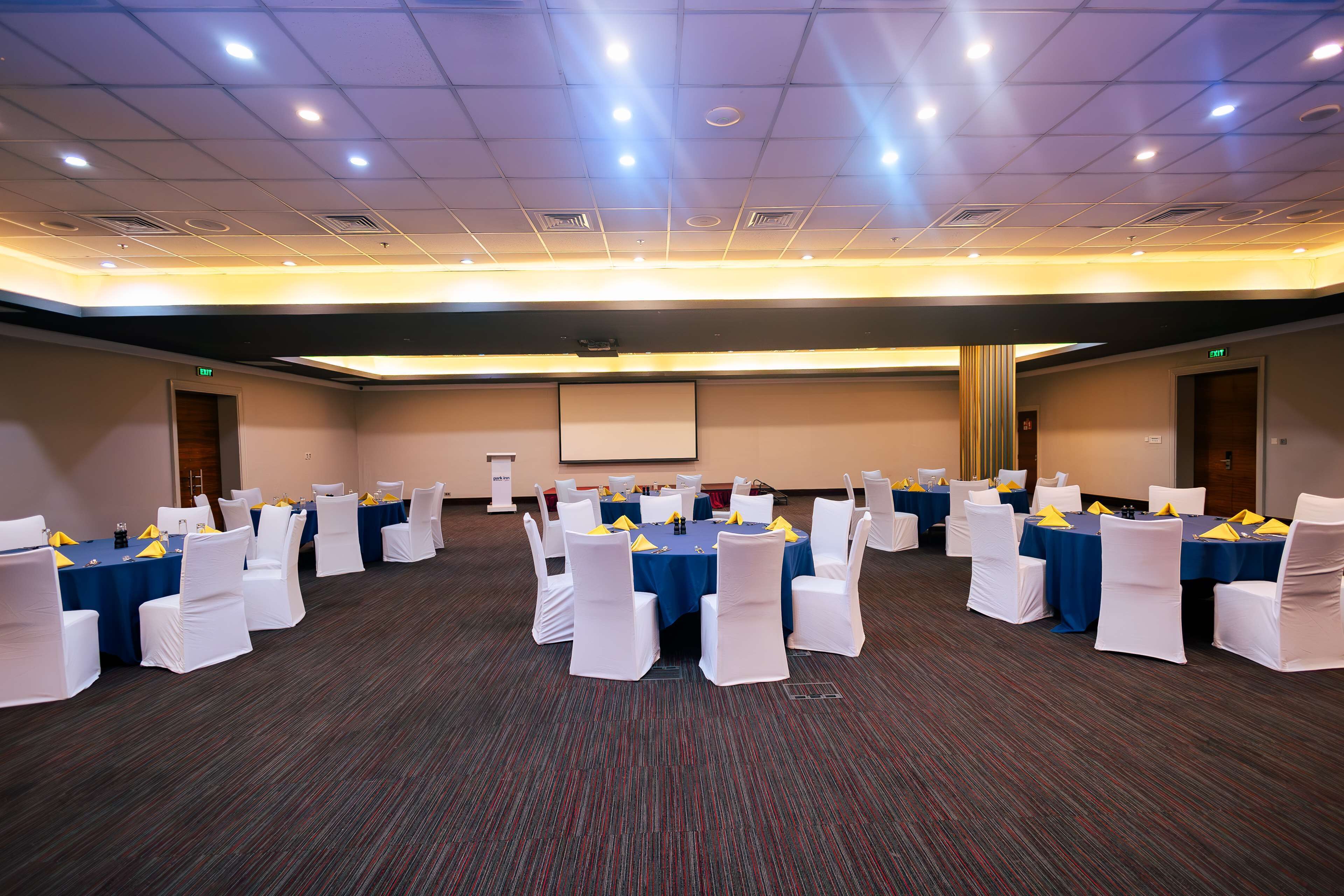 Un salón de conferencias con varias mesas y sillas, equipado con proyectores y pantallas.