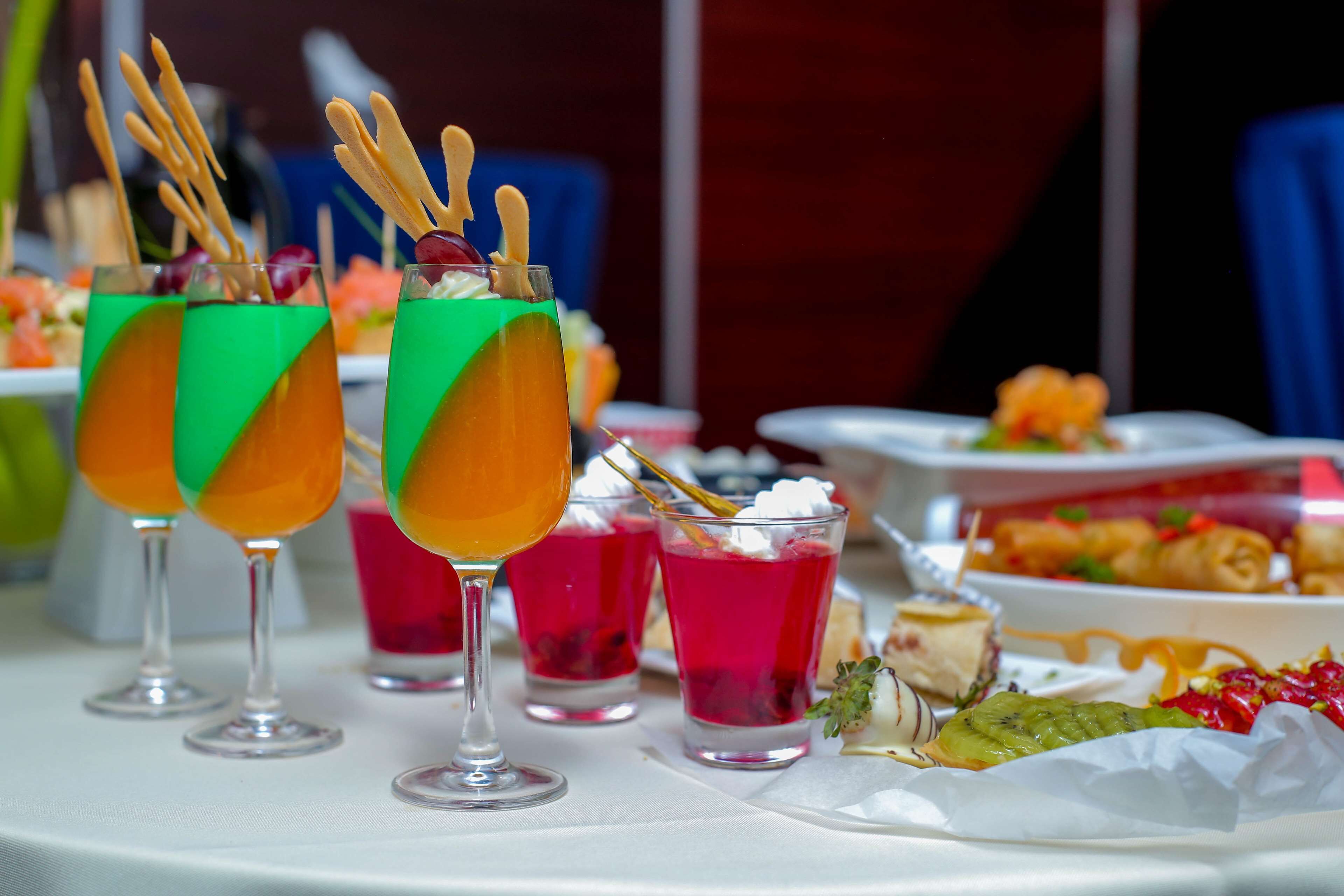 Una mesa con diversas bebidas en vasos, algunas con palitos de madera, y una variedad de postres.