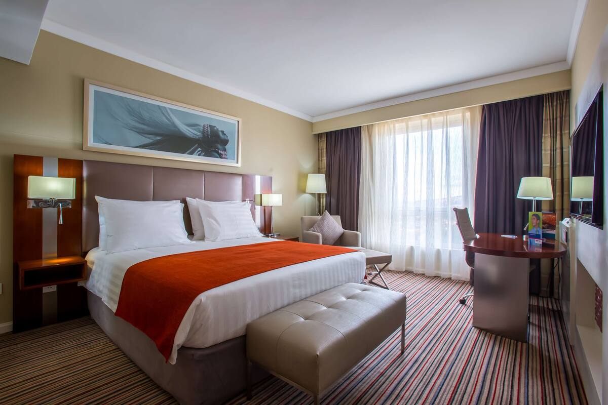 A hotel room with a large bed, a desk, a chair, and a television.