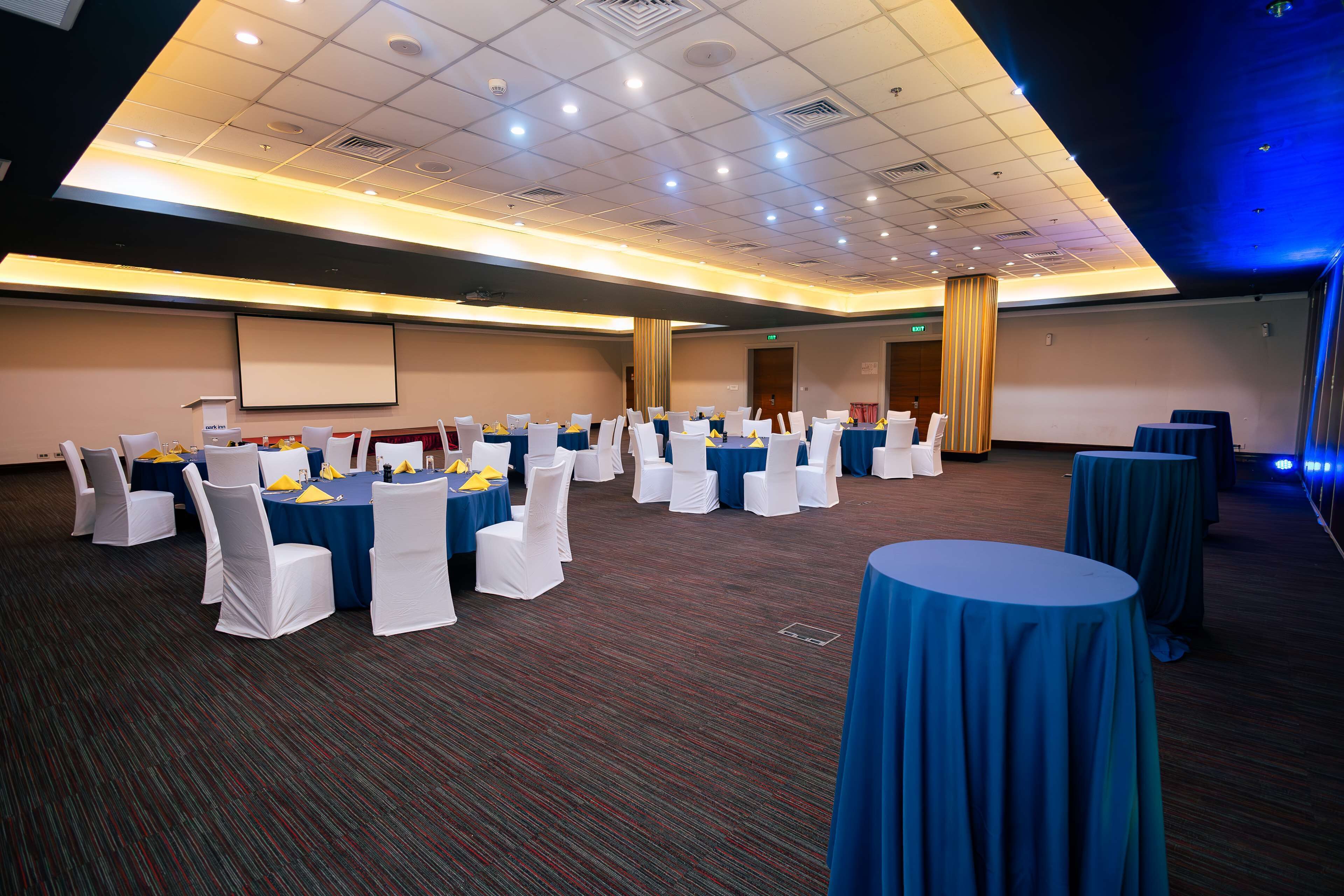 A conference room with round tables, white chairs, and blue tablecloths.