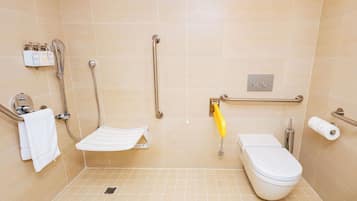 Ein Badezimmer mit Dusche, Toilette, Haltegriffen und Handtuchhalter.