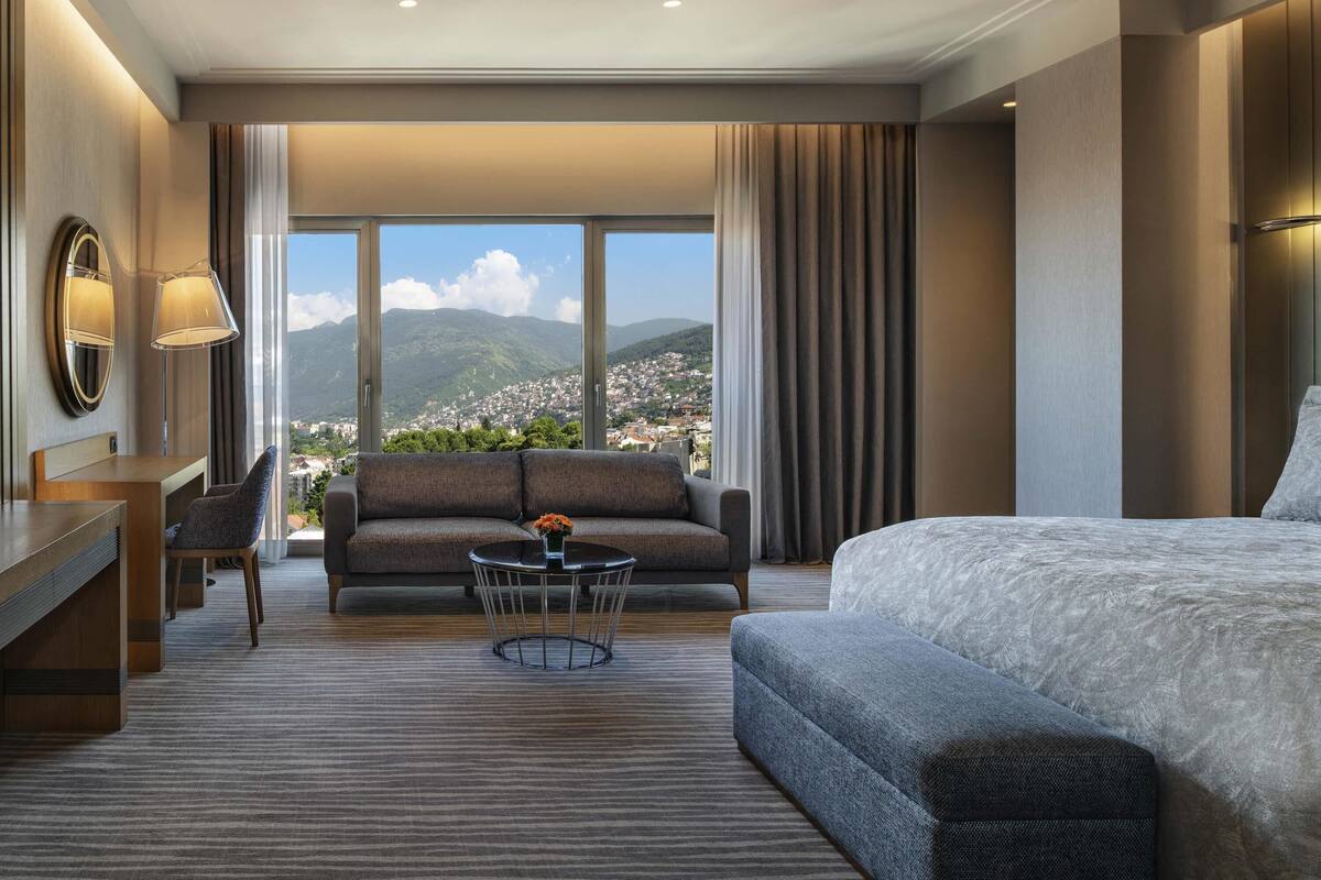Une chambre d’hôtel équipée d’un lit, d’un canapé, d’un bureau et offrant une vue sur la ville et les montagnes.