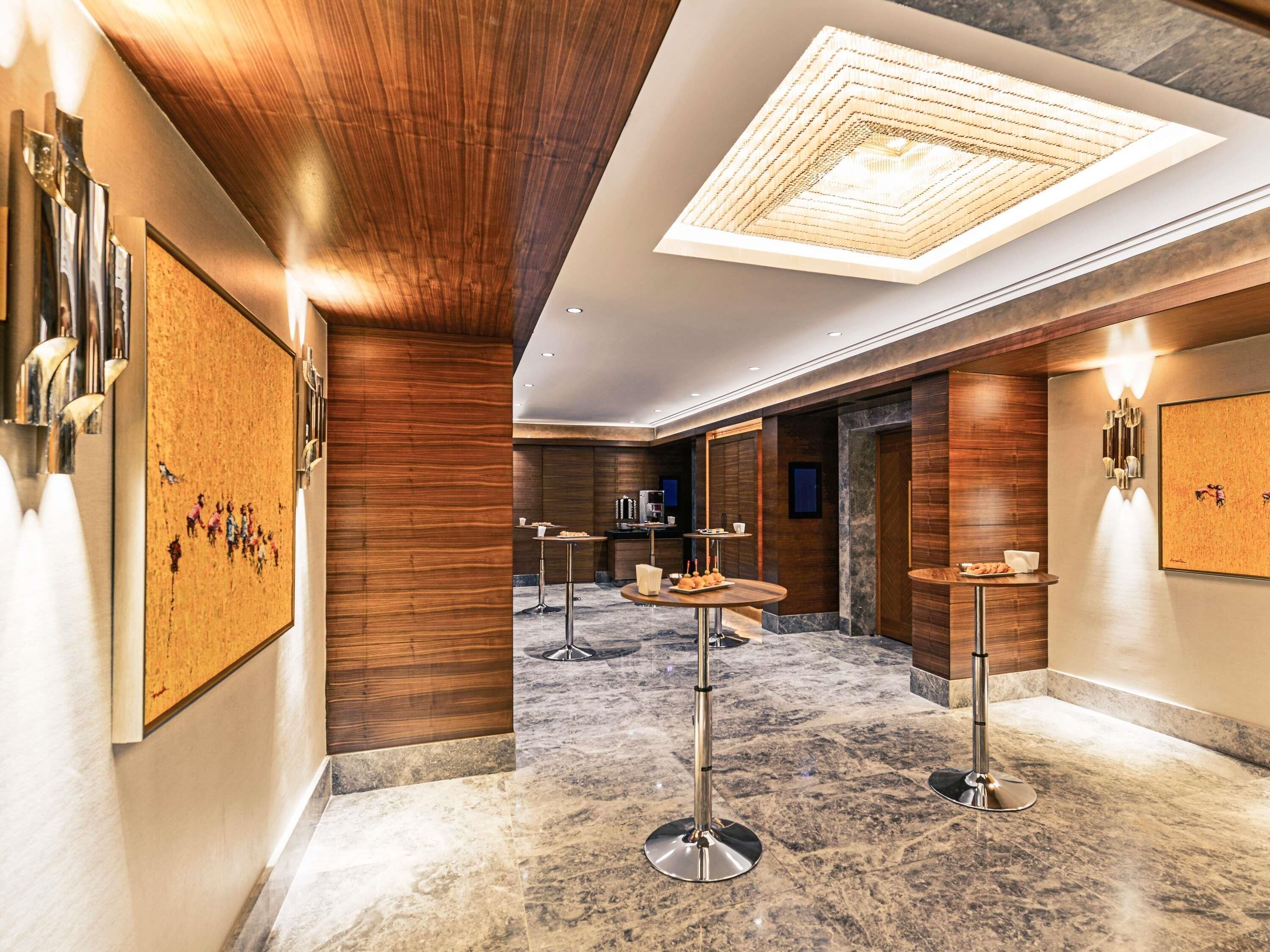 A modern hotel lobby with wooden paneling, a central round table, and a ceiling light fixture.