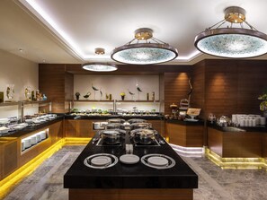 A buffet setup with multiple serving stations, a central dining table with plates, and overhead lighting fixtures. - Mövenpick Hotel & Thermal Spa (Bursa)