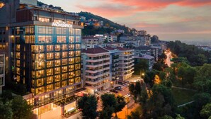 Un hotel moderno con varios pisos, grandes ventanales y una terraza en la azotea.