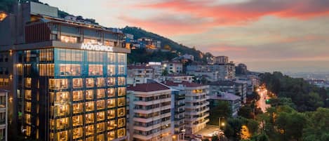 Un hotel moderno con varios pisos, grandes ventanales y una terraza en la azotea.