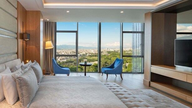 Habitación de hotel moderna con una cama grande, dos sillas azules, una mesita y un televisor.