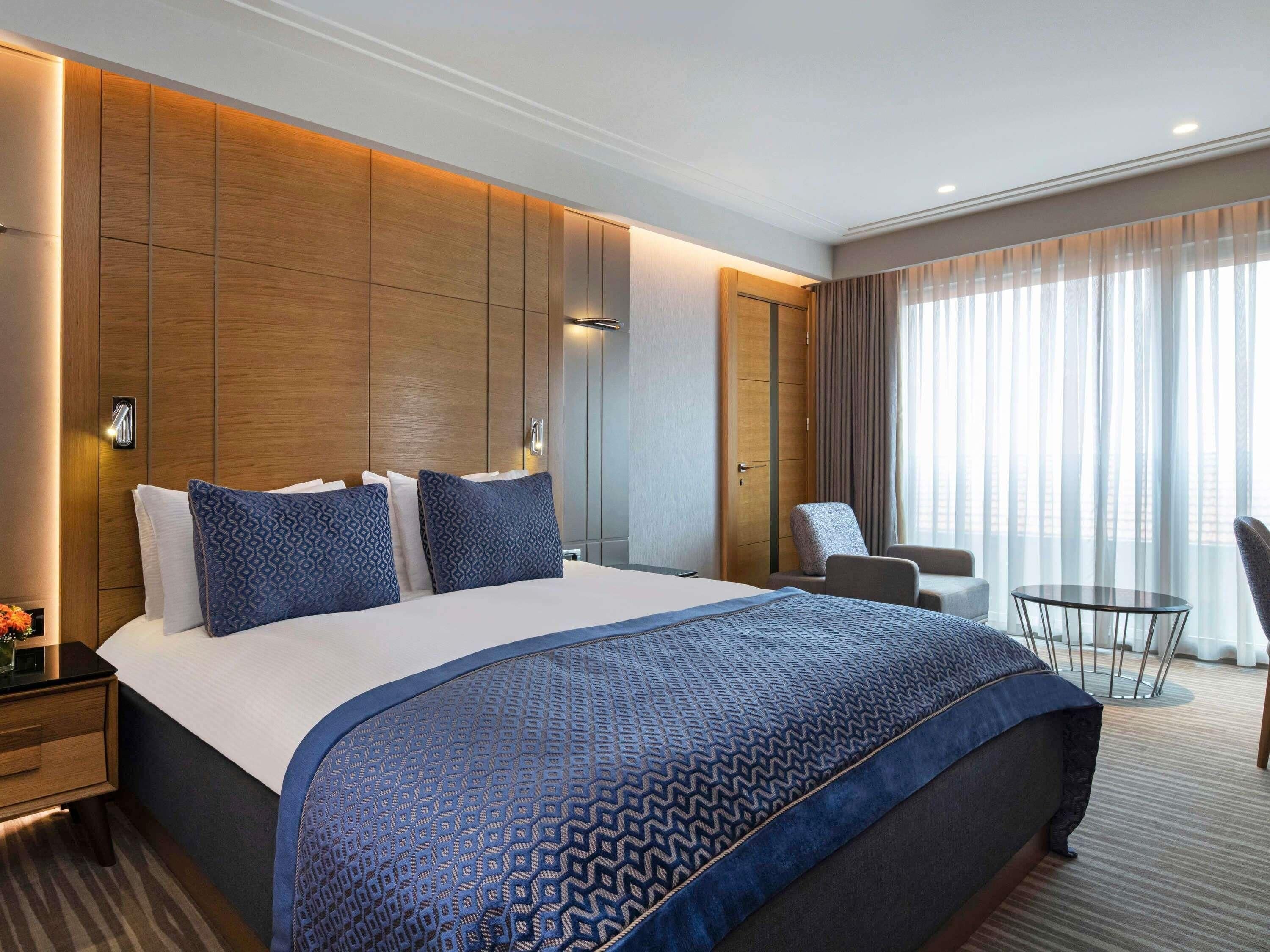A hotel room with a large bed, a desk, a chair, and a small table.