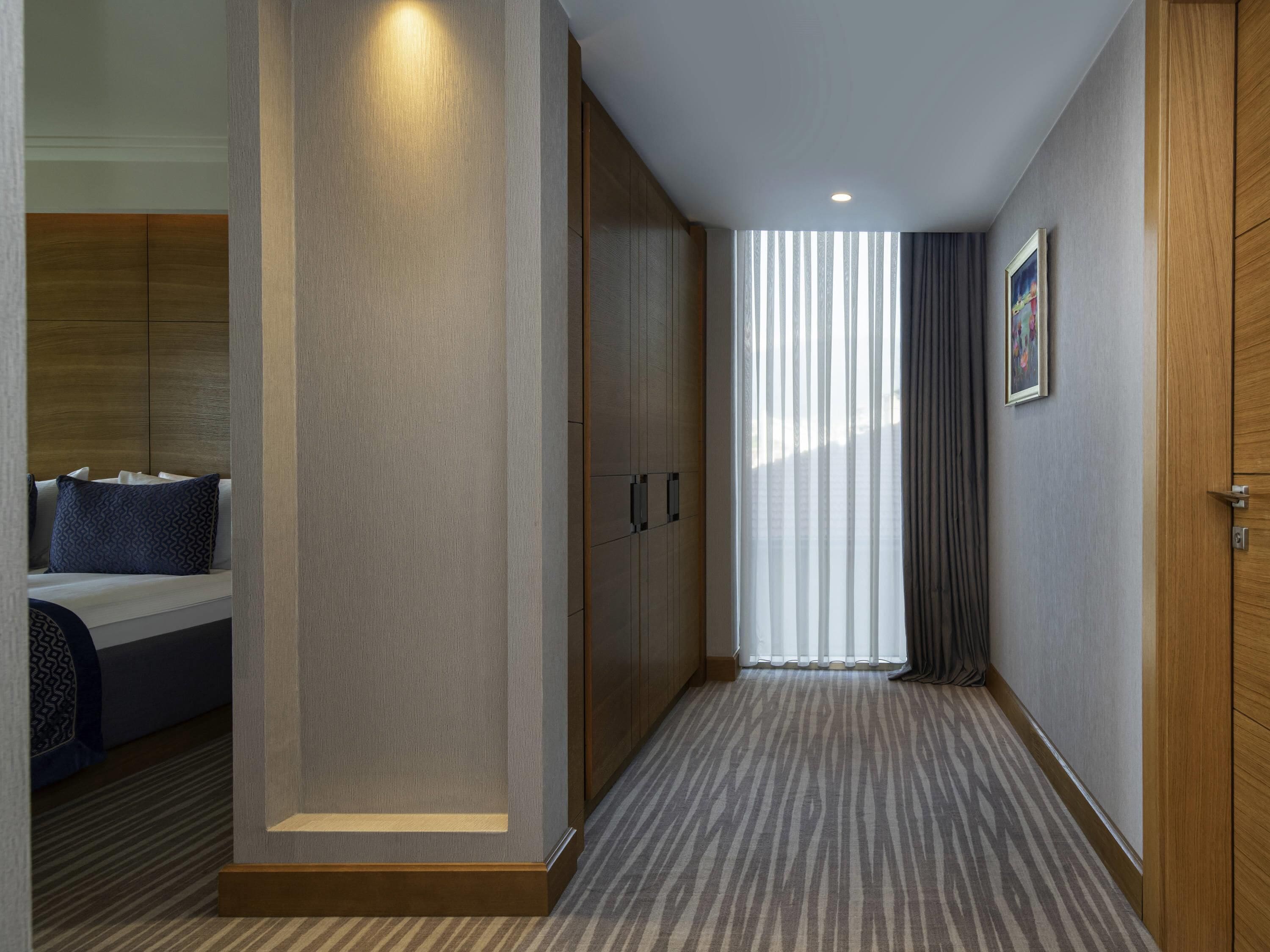 A hotel room with a bed, a wardrobe, a mirror, and a window with curtains.