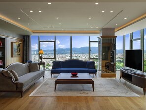 A spacious living room with a sofa, coffee table, and TV, large windows with a city view, and a bookshelf. - Mövenpick Hotel & Thermal Spa (Bursa)