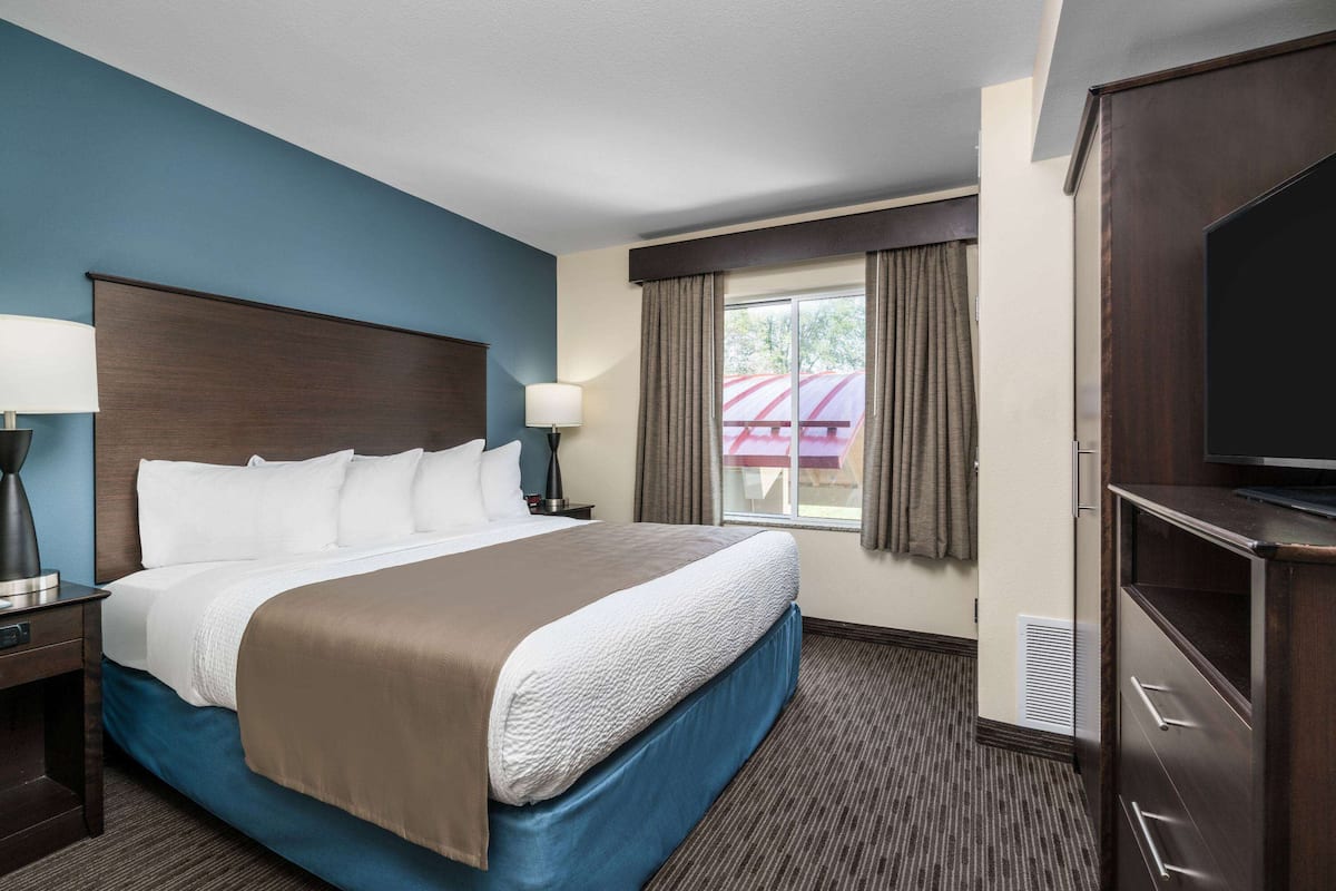 A hotel room with a large bed, a TV, a desk, and a window with curtains.