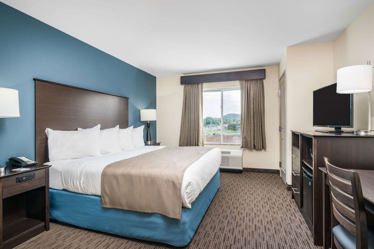A hotel room with a bed, desk, chair, and a window with curtains.