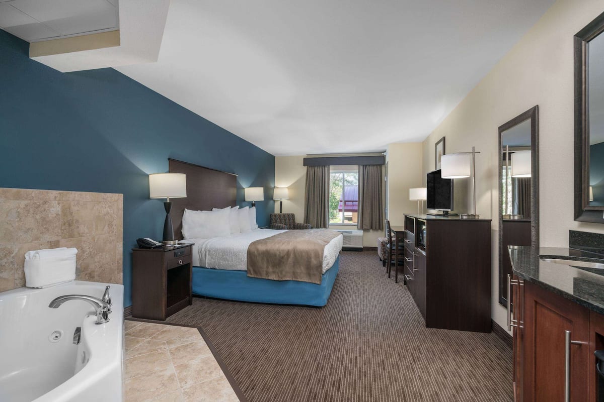 A hotel room with a large bed, a separate bathroom with a bathtub, a desk with a chair, and a large mirror.