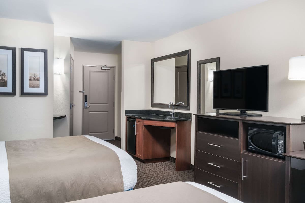A hotel room with two beds, a desk with a sink, a television, and a microwave.