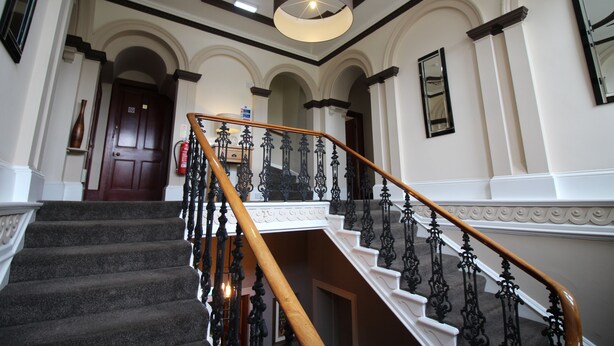 A grand staircase with ornate black railings and a wooden handrail, leading to a landing with a white balustrade.