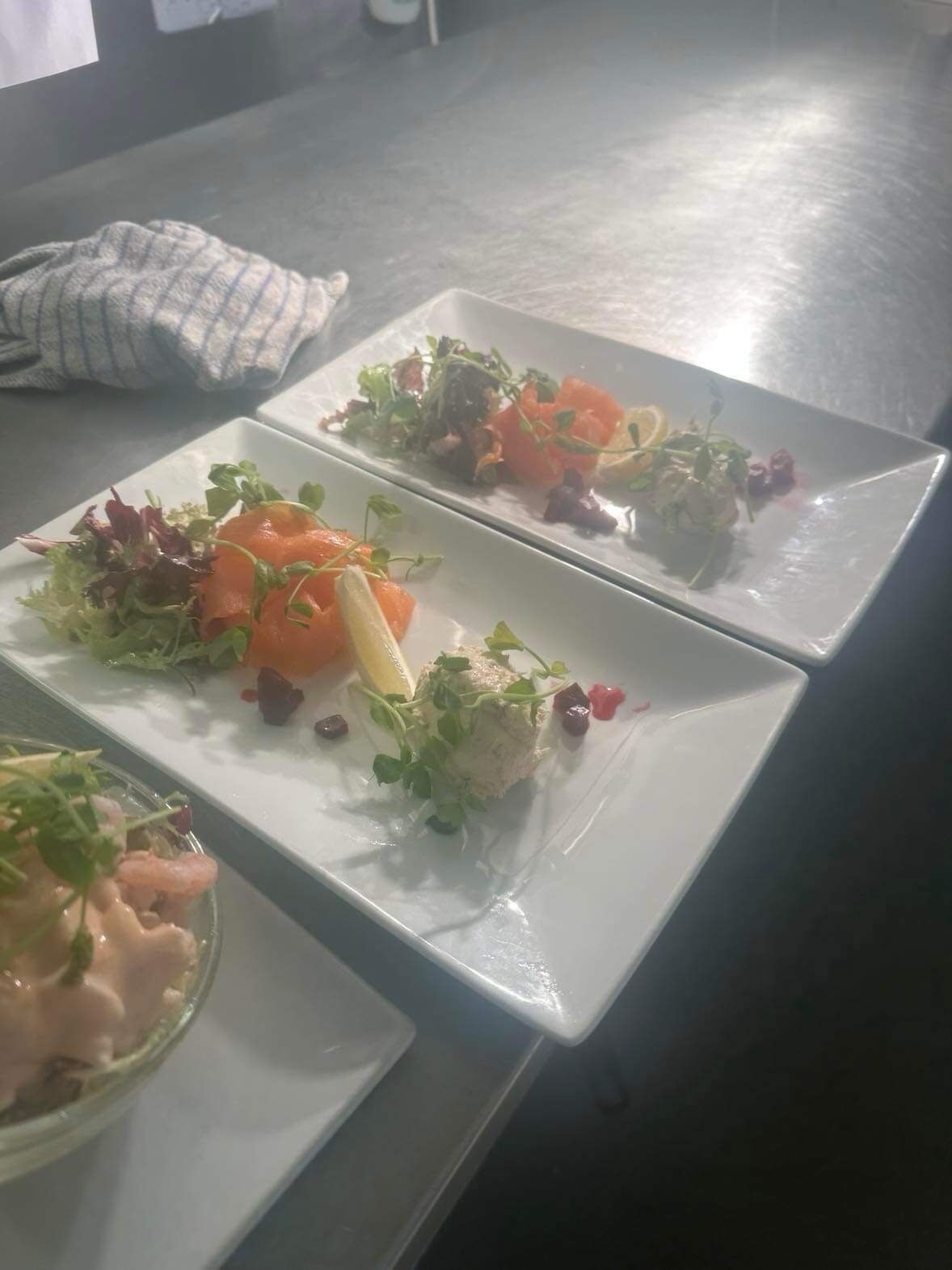 Una mesa de comedor con tres platos cuadrados de comida, cada uno con diferentes preparaciones.