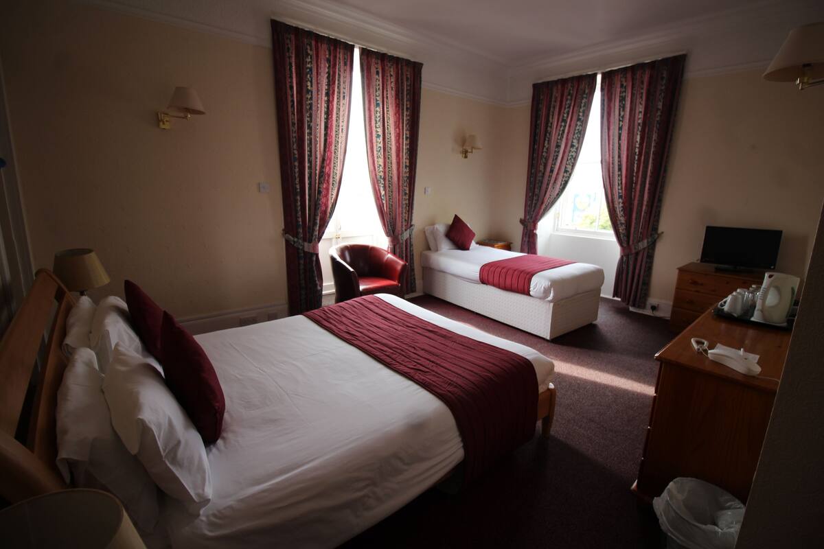 Ein Hotelzimmer mit einem großen Bett, einem Schlafsofa, einem Sessel, einem Schreibtisch mit Lampe und einem Fernseher.