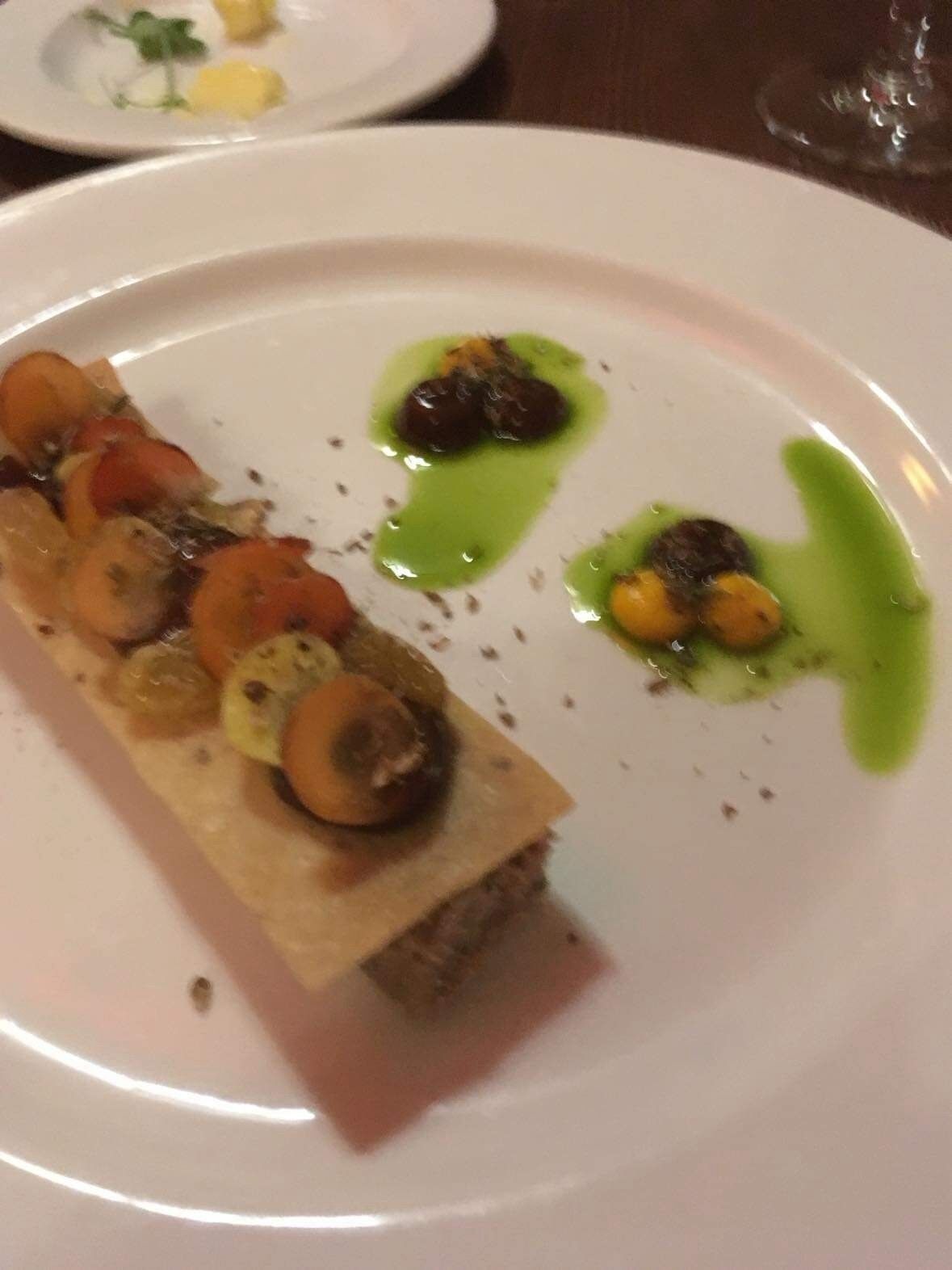 A white plate with a rectangular dish topped with vegetables and a green sauce.