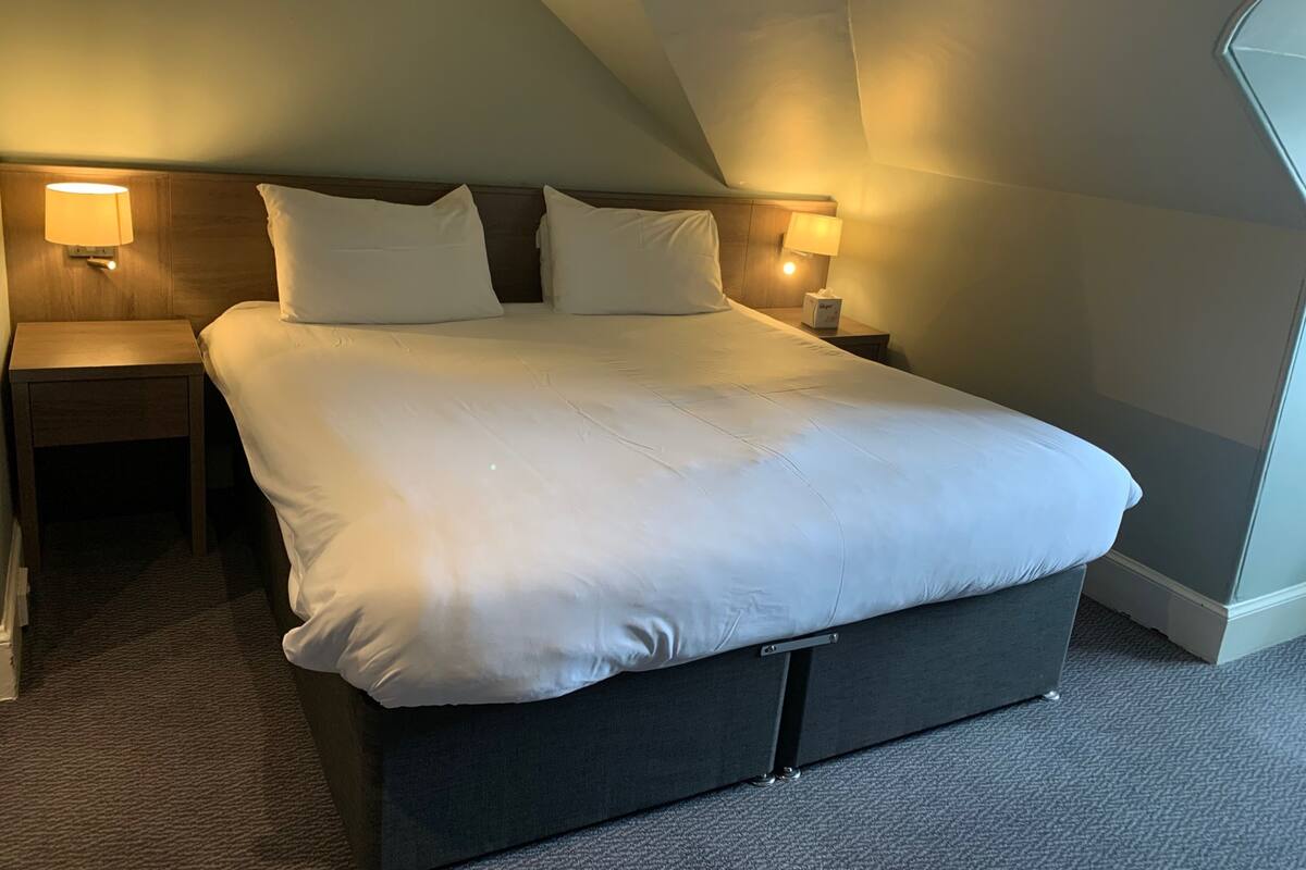 Ein Hotelzimmer mit einem großen Bett, zwei Nachttischen mit Lampen und einem Teppichboden.