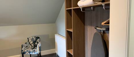 A room with a chair, a wooden closet with shelves, and a radiator.