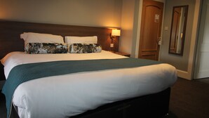 A hotel room with a large bed, a nightstand, a lamp, and a door.