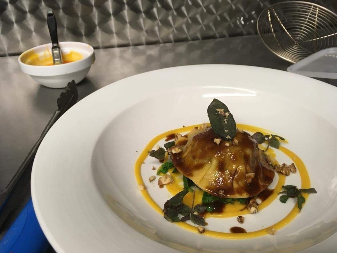 A white plate with a dish of food, a small bowl with sauce, and a whisk in the background.