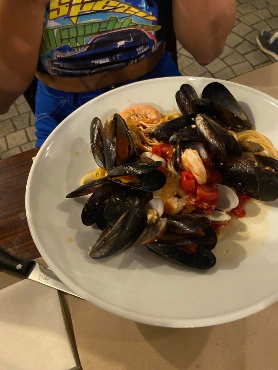 A plate of mussels with shrimp and tomatoes on a white plate.