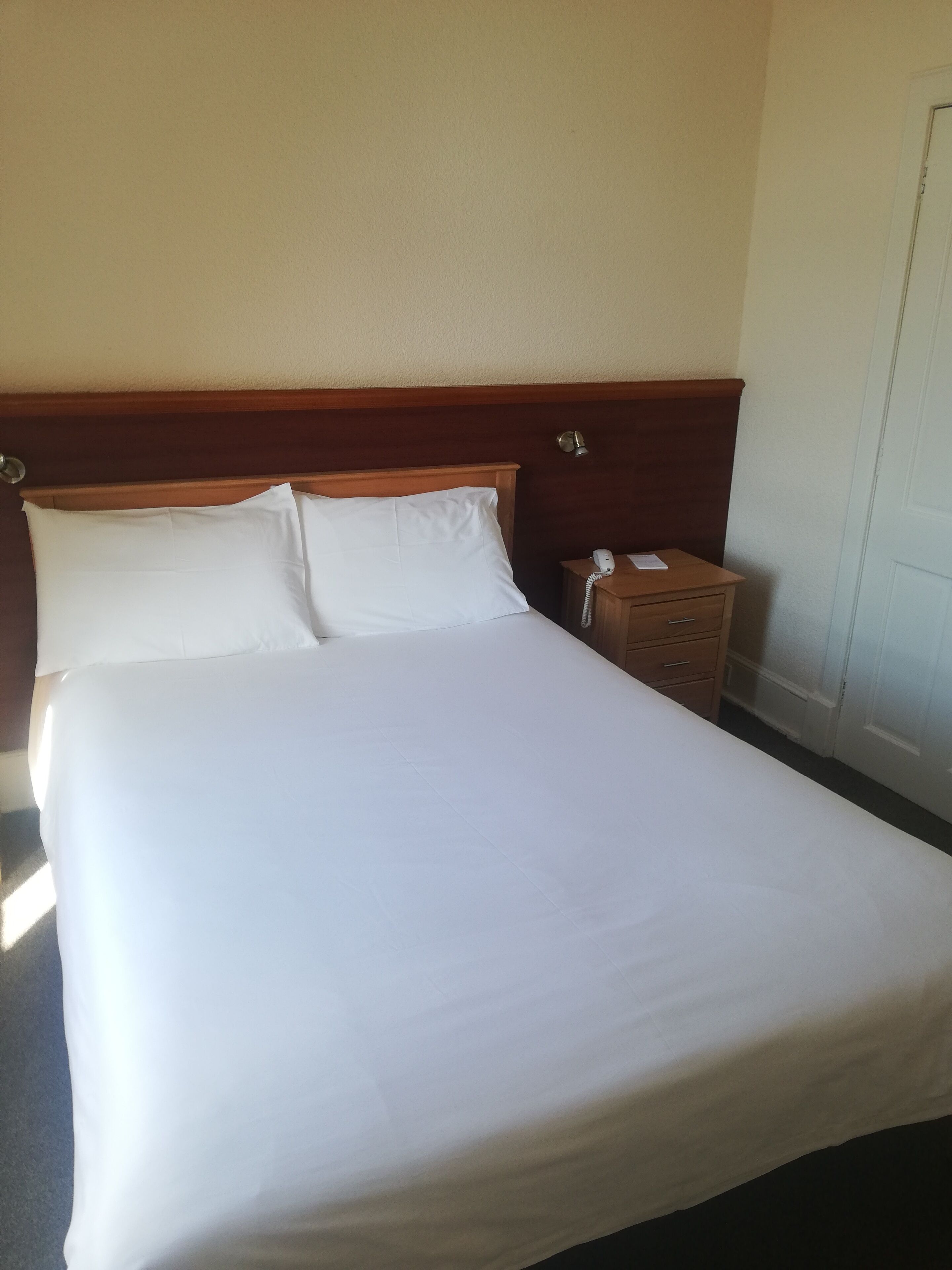 A neatly made bed with white linens in a hotel room.