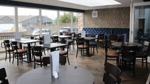 A restaurant with multiple tables and chairs, large windows, and a view of the parking lot.