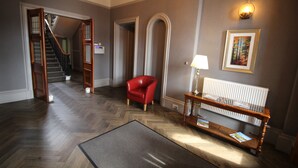 A spacious hallway with a herringbone floor, a red chair, a wooden console table with magazines, and a framed picture on the wall.