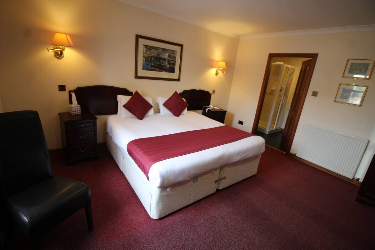 Ein Hotelzimmer mit einem großen Bett, zwei Nachttischen, einem Sessel, einem Spiegel und einem gerahmten Bild an der Wand.