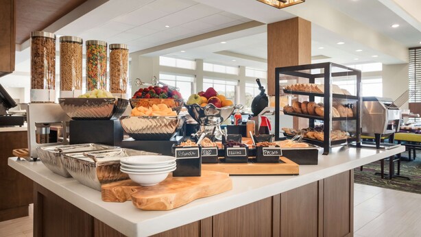 Un espace buffet proposant différents stands de nourriture, chacun étant clairement identifié, et où l’on trouve notamment des fruits, du granola et des viennoiseries.