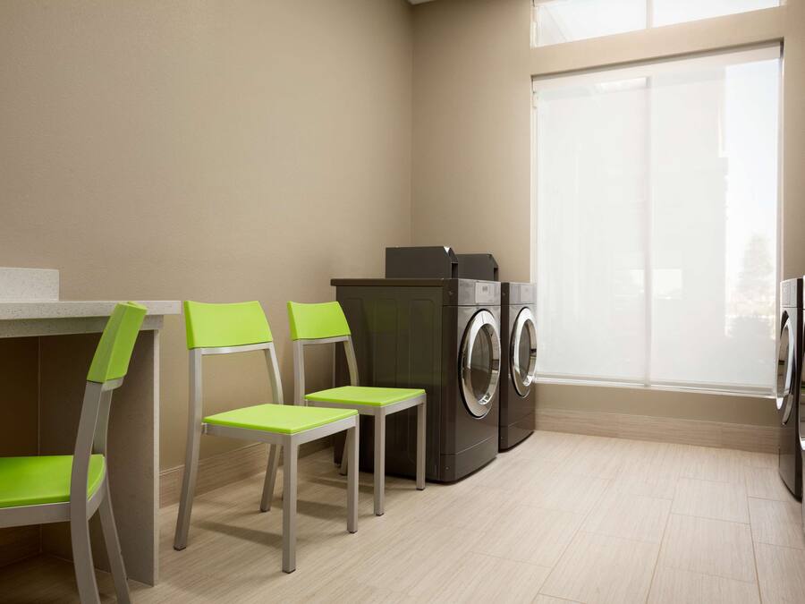 A laundry room with two washing machines, two chairs, and a window.