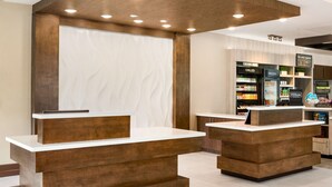 Un espace d’accueil d’hôtel avec des comptoirs de réception en bois et un présentoir de boissons fraîches et surgelées.