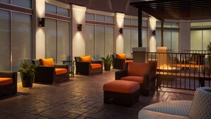 Un espace patio extérieur moderne, doté de meubles en osier et de coussins orange, d’un foyer et de grandes fenêtres.