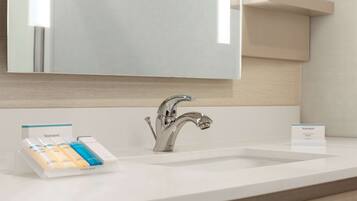 A modern bathroom with a white sink, a chrome faucet, and a mirror above. There are two Neutrogena soap dispensers on the sink.