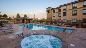 A hot tub surrounded by lounge chairs and a pool area with a view of mountains.
