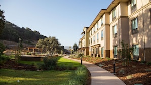 A residential building with a pathway leading to a covered area, surrounded by greenery and a hilly landscape.