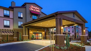 A Hampton Inn & Suites hotel with a covered entrance, outdoor seating area, and landscaped garden.