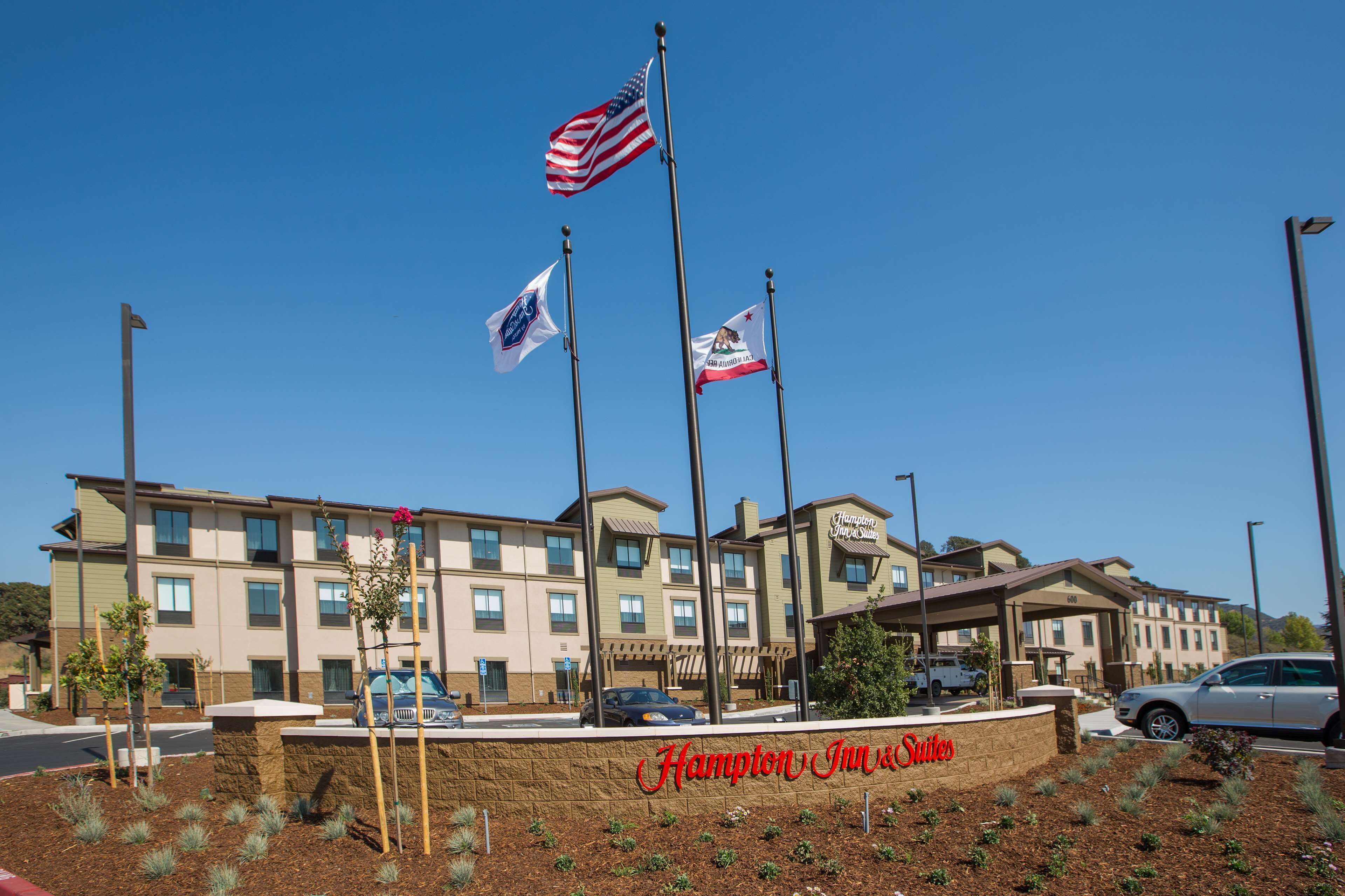 A hotel with multiple flags, a clear sky, and a sign reading "Hampton Inn & Suites".