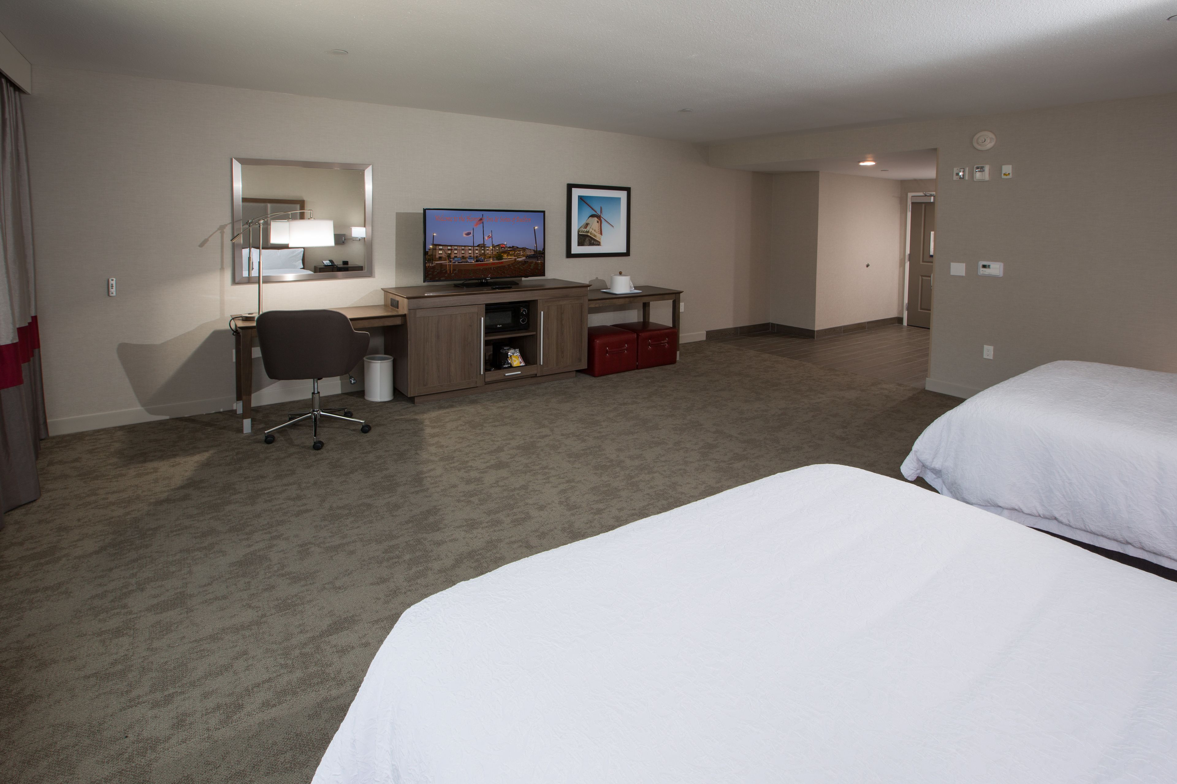 Ein Hotelzimmer mit zwei Betten, einem Schreibtisch mit Computer, einem Sessel, einem Fernseher und einer kleinen Küchenzeile.