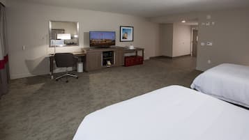 A hotel room with two beds, a desk with a computer, a chair, a TV, and a small kitchenette.