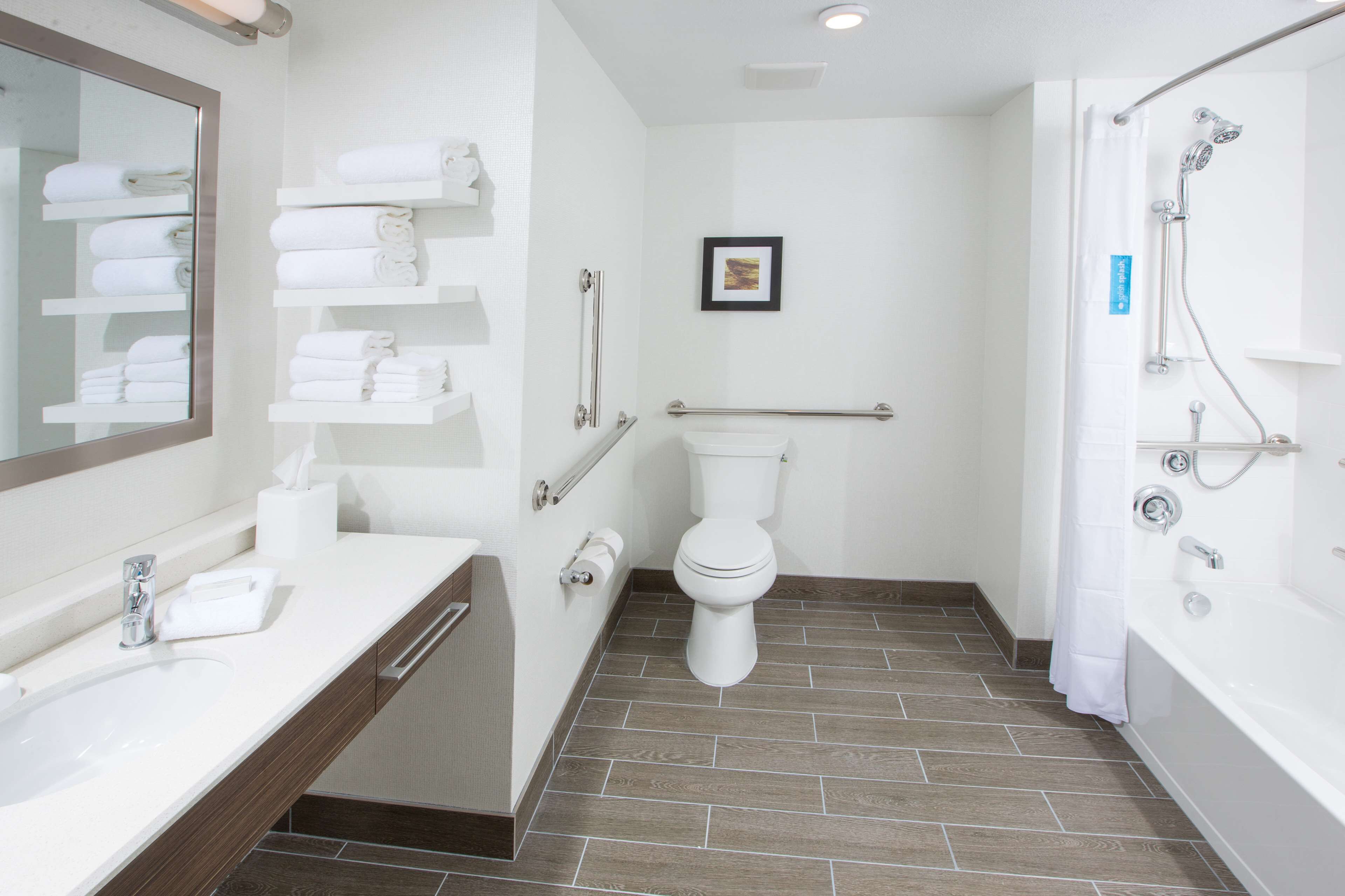 A modern bathroom with a sink, toilet, and shower. There are shelves with towels and a framed picture on the wall.